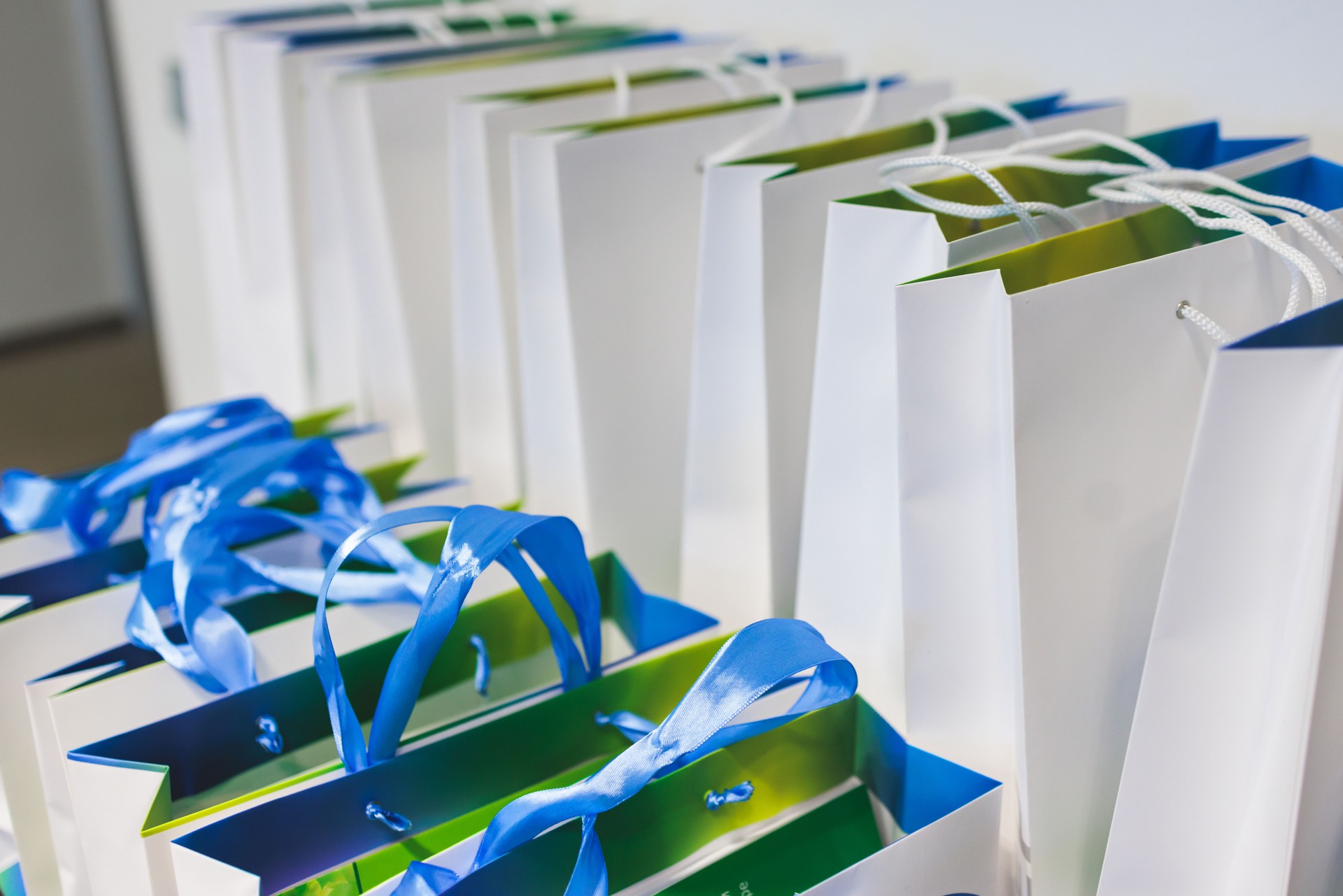 Corporate gifts and souvenirs presentation for company employees, gift bag package for conference participants before start, gift giving at office work, white and green paper bags with a blue ribbon